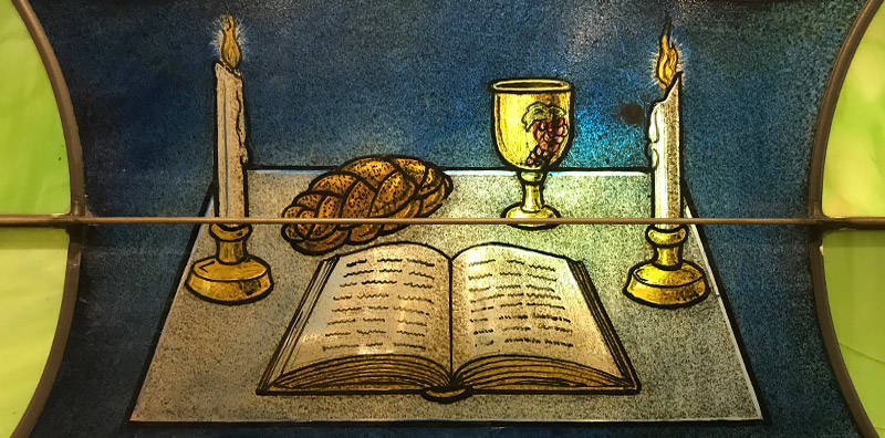 Stained glass window depicting the book (Torah), two candles, a cup (kiddush) and a loaf of bread (challah)